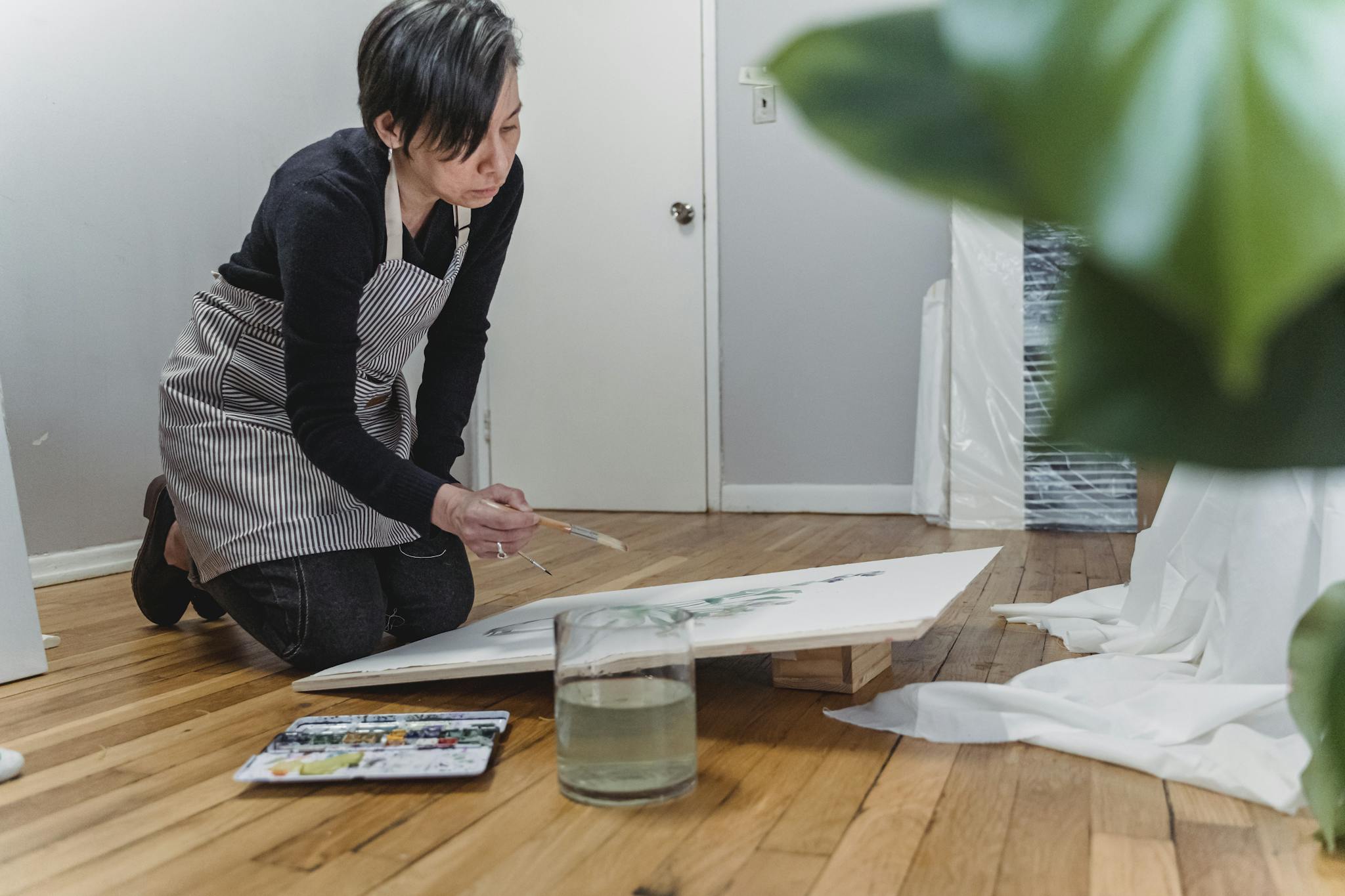 A woman artist focuses on painting a canvas in her home studio, showcasing creativity.