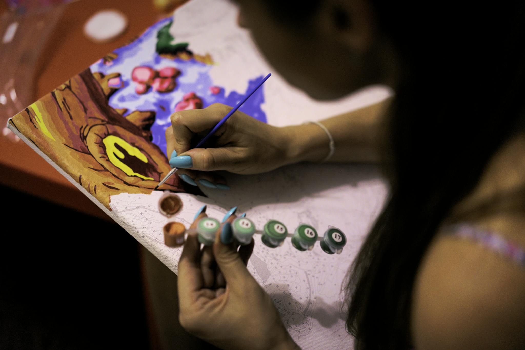 A woman engages in a relaxing hobby, painting a vibrant picture by numbers.
