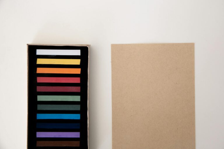 A box of colorful pastel sticks alongside a blank sheet on a white background, perfect for creative projects.