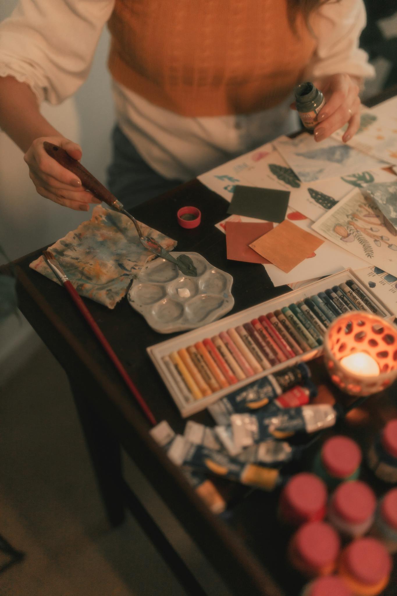 A cozy art workspace with candles, paints, and tools, fostering a creative and warm atmosphere.