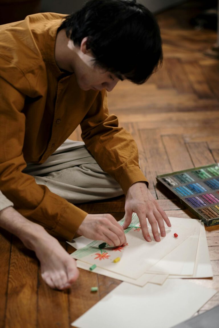 A man focuses on drawing with pastels on paper, capturing the essence of creativity and focus.