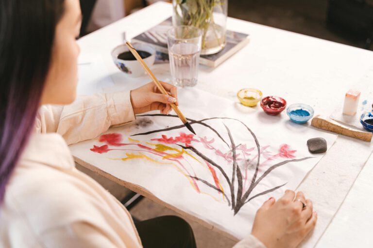 A woman using watercolors to paint floral art indoors at a creative workspace.