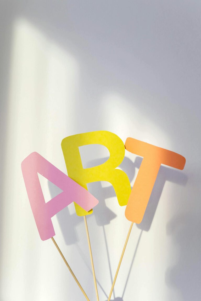 Vibrant paper cutouts spelling 'ART' in pastel tones on a soft-lit background.